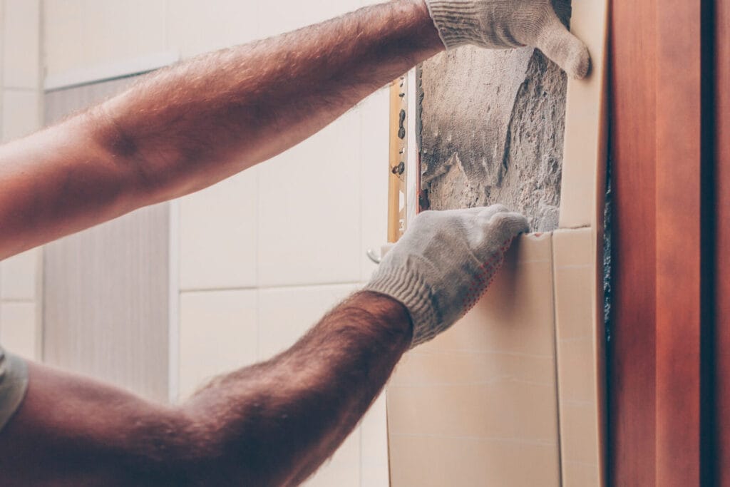 A mann working with his hands carefully removes old tiles from the wall.